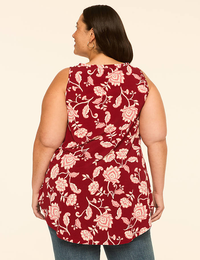 A woman in a floral print top stands against a plain, light-colored background.