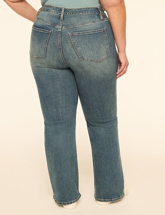 A person wearing blue jeans stands against a plain, light-colored background.