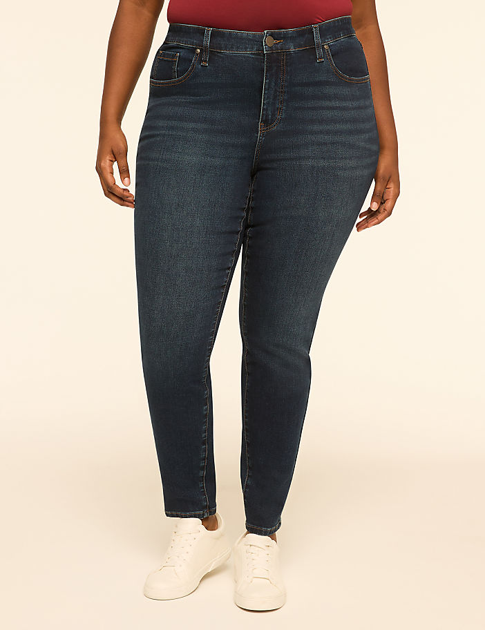 A person stands in dark wash skinny jeans and white sneakers against a plain, light-colored background.