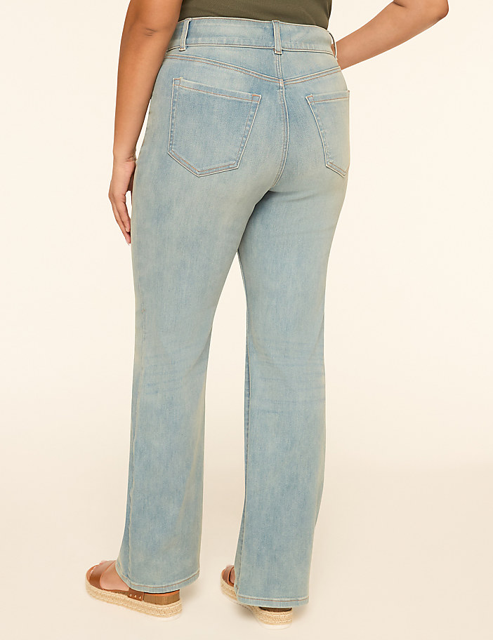 A person wearing light wash bootcut jeans and sandals stands against a plain, light-colored background.