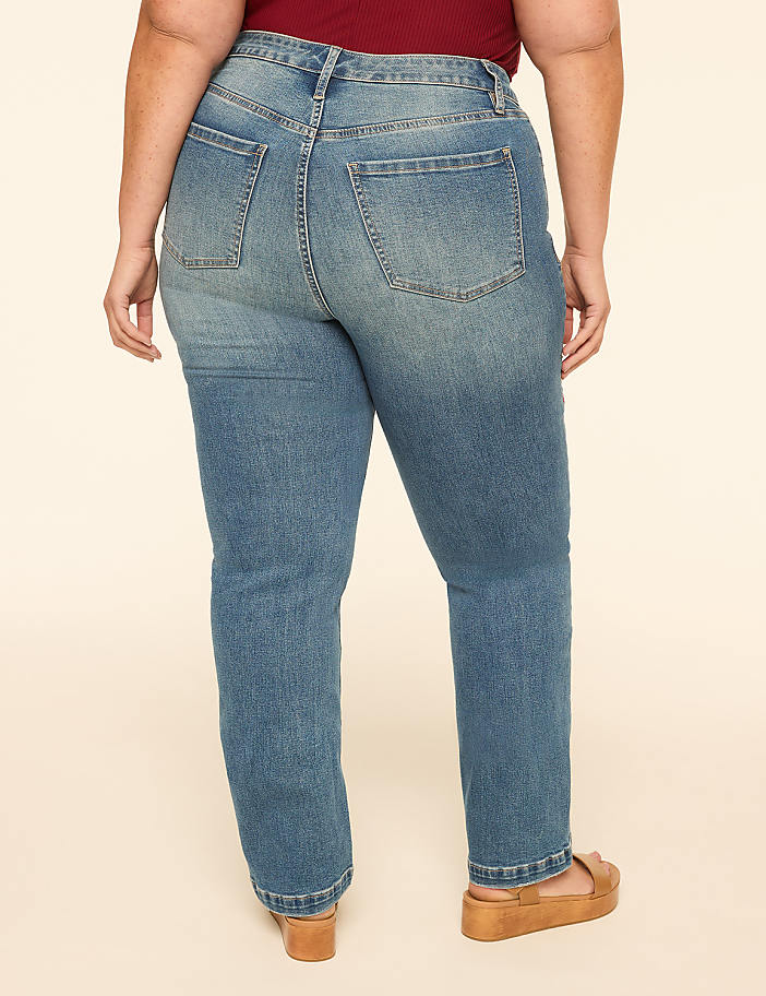 A person wearing blue jeans and tan platform sandals stands against a plain cream background.