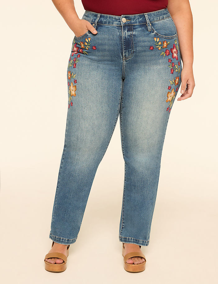 A woman in embroidered jeans stands against a plain, light-colored background.