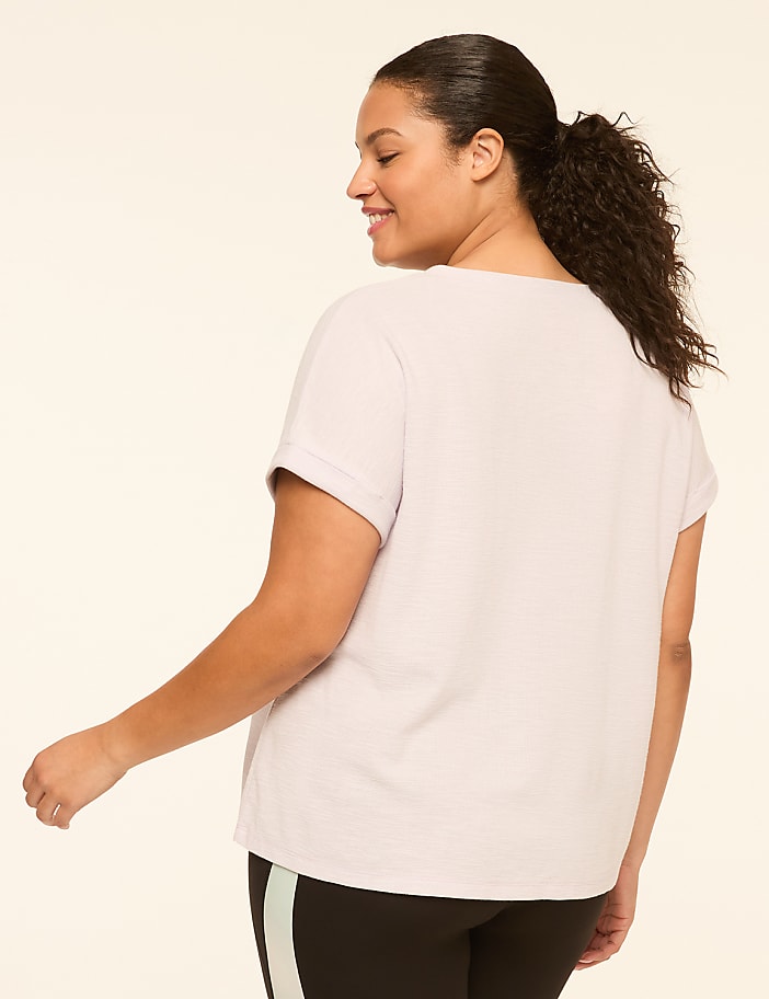 A woman in a light purple t-shirt and black leggings with a stripe stands against a plain, light-colored background.