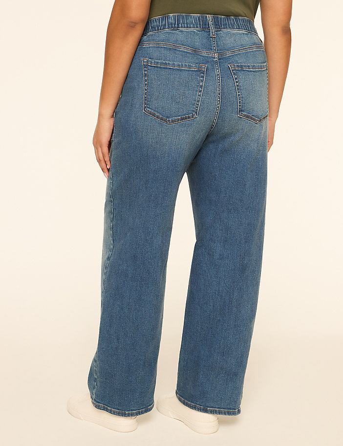 A person wearing wide-leg blue jeans stands against a plain, light-colored background.