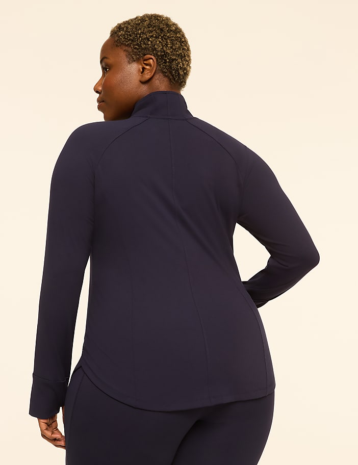 A woman in a navy blue jacket and leggings stands against a plain beige background.