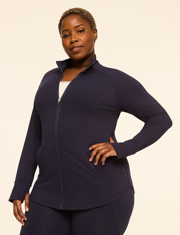 A woman in a navy blue zip-up jacket and matching pants stands against a plain, light-colored background.