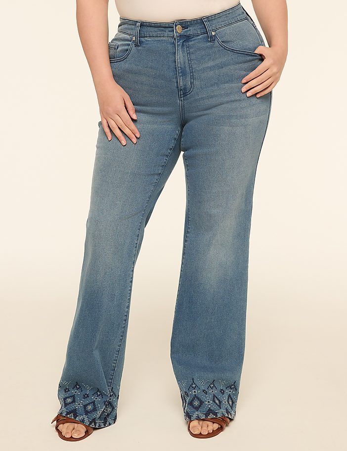 A person wearing light blue flared jeans with embroidered hems stands against a plain, light-colored background.