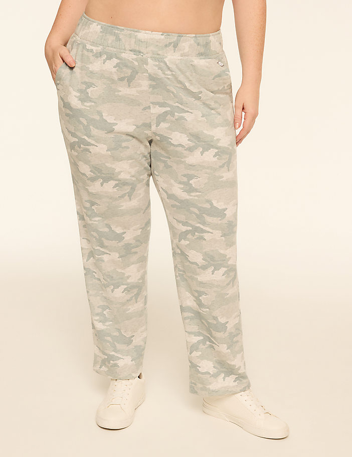 A person stands in camouflage pants and white sneakers against a plain, light-colored background.