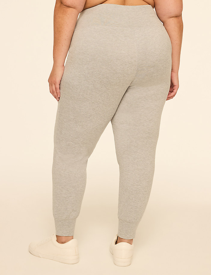 A person wearing grey sweatpants and white sneakers stands against a plain beige background.