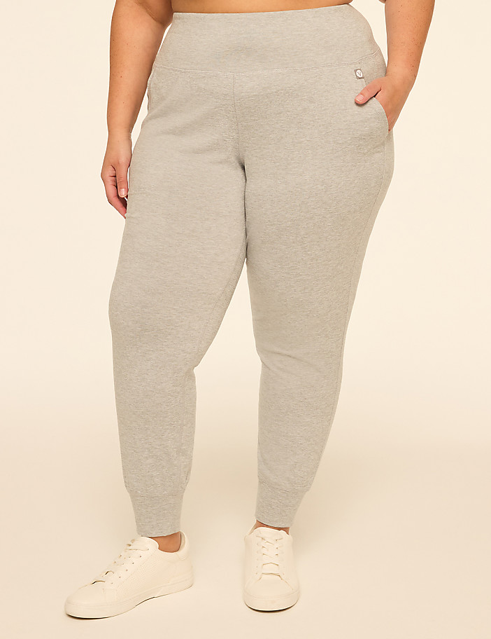 A person wearing grey sweatpants and white sneakers stands against a plain, light-colored background.