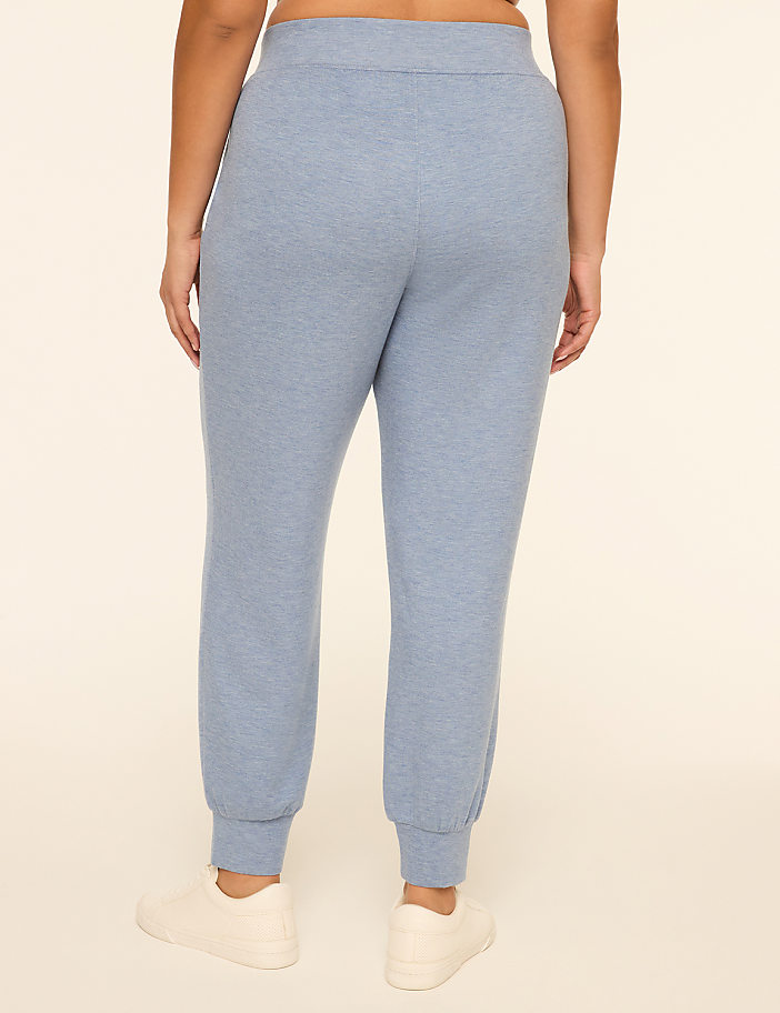 A person wearing light blue sweatpants and white sneakers stands against a plain, light-colored background.