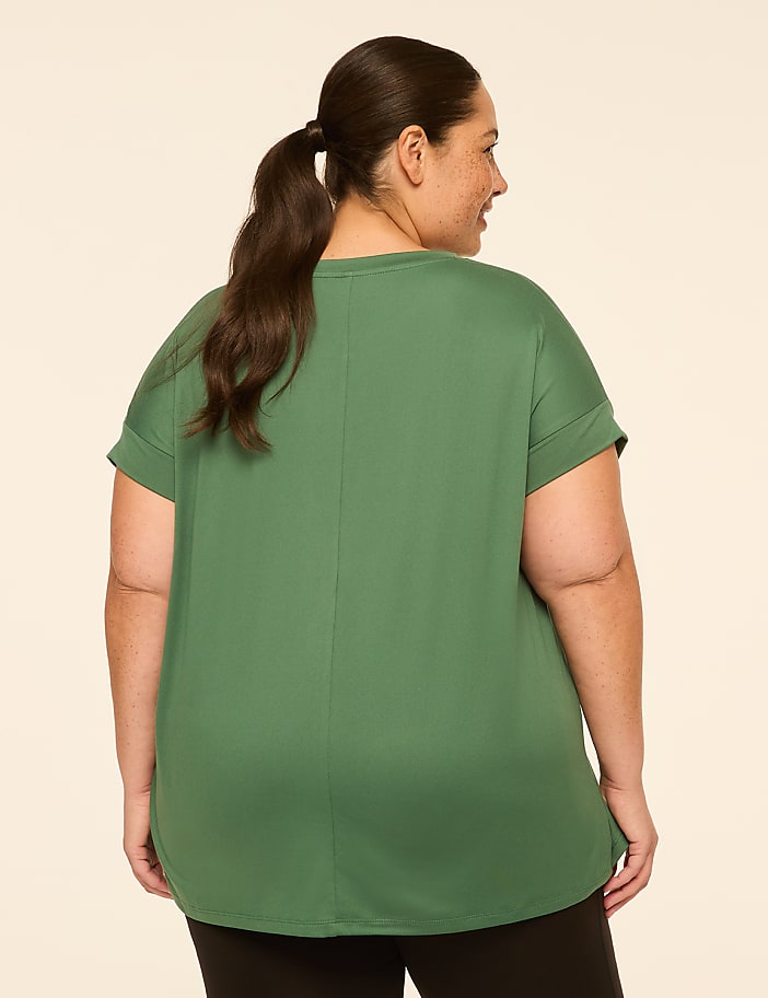 A woman with dark hair pulled into a ponytail, wearing a green t-shirt, stands against a plain, light-colored background.