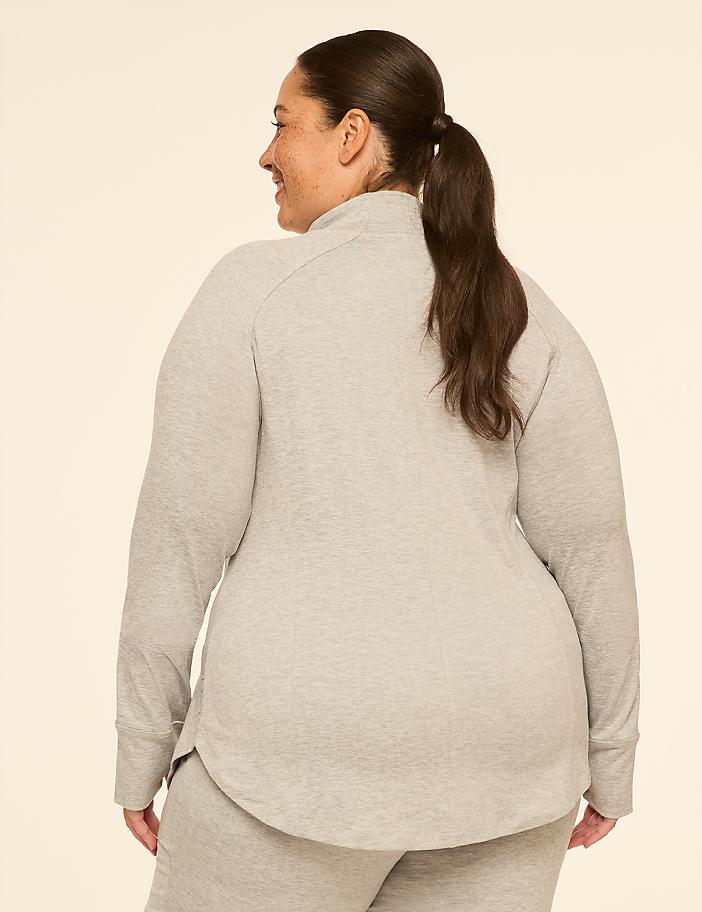 A woman in a grey sweatshirt and sweatpants stands facing away from the camera against a plain, light-colored background.