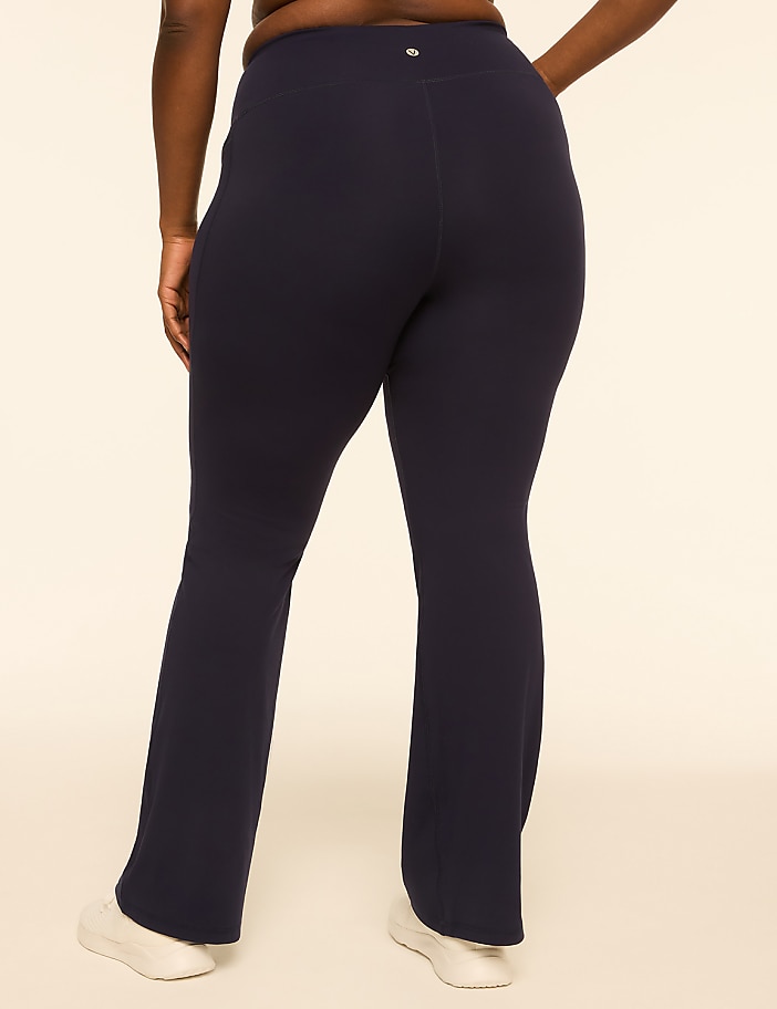 A person wearing navy flare leggings and white sneakers stands against a plain, light-colored background.