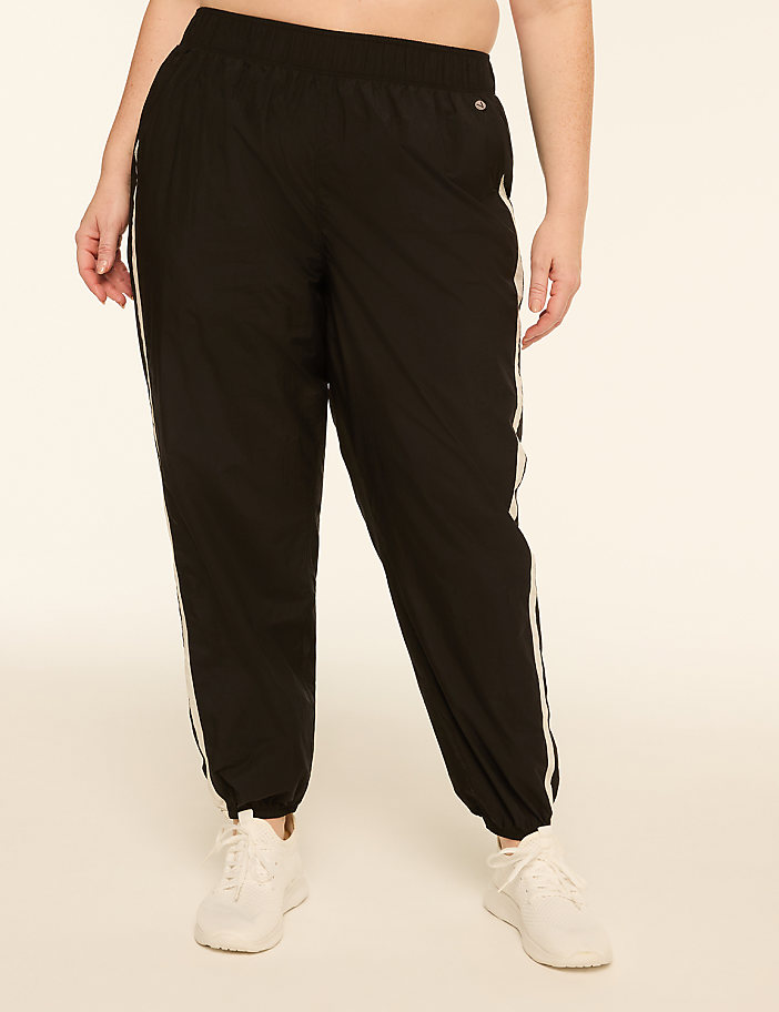 A person stands in black track pants with white stripes and white sneakers against a plain, light-colored background.