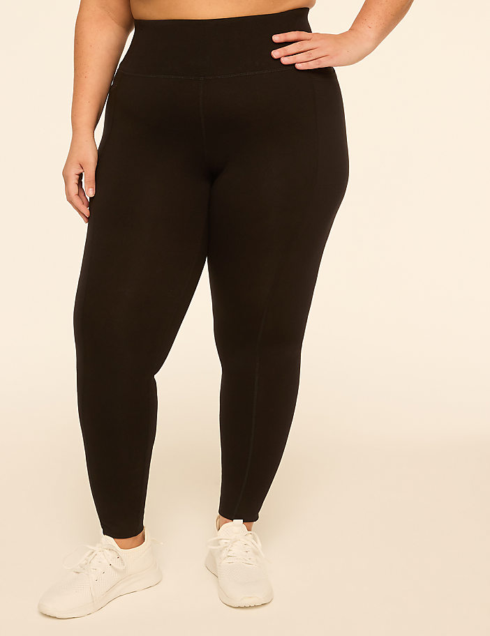 A person wearing black leggings and white sneakers stands against a plain, light-colored background.