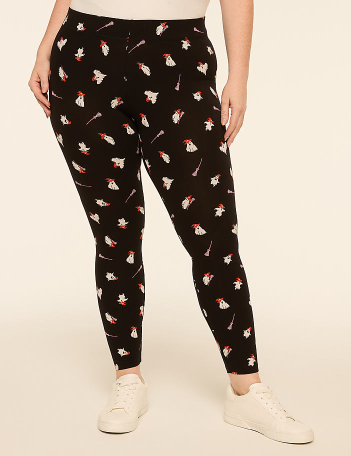 A person wearing black leggings with a white and red ghost pattern stands against a plain, light-colored background.