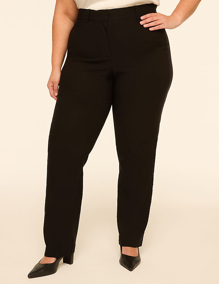 A person in black pants and black heels stands against a plain, light-colored background.