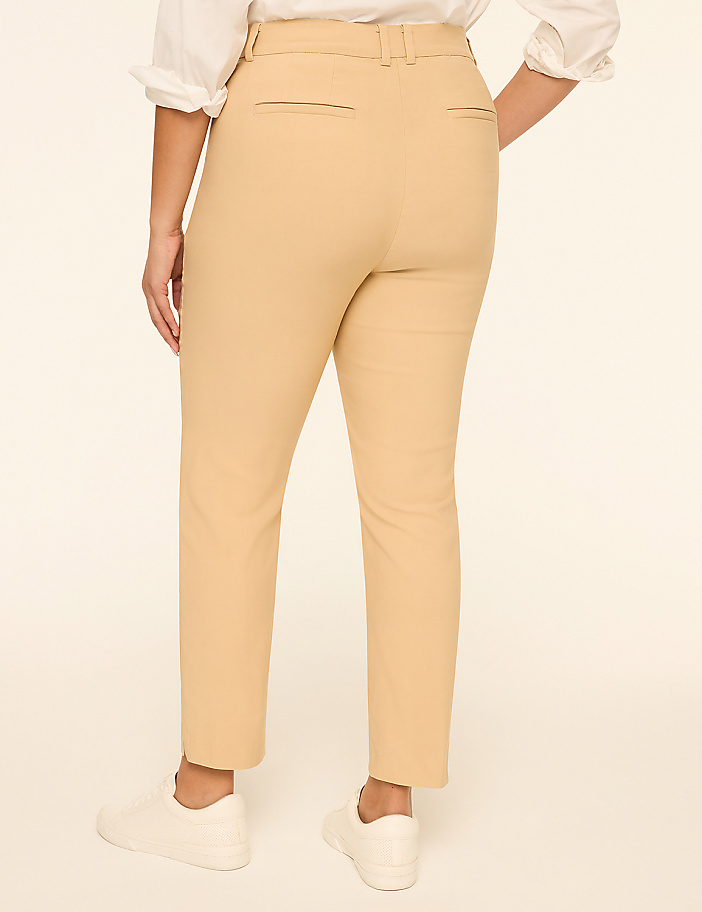 A person wearing tan pants and white sneakers stands against a plain, light-colored background.