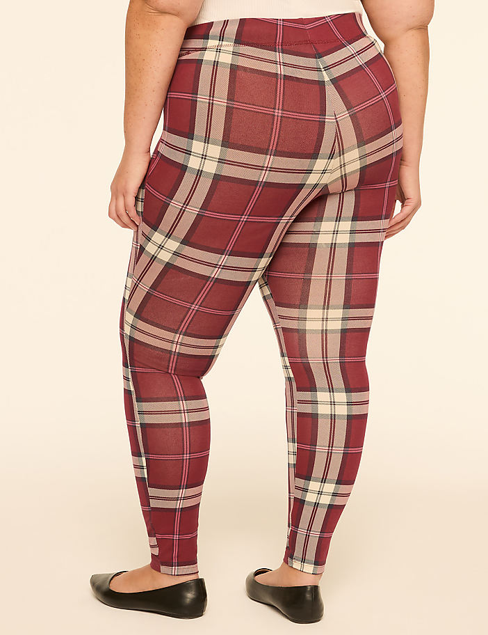 A person wearing plaid leggings and black flats stands against a plain, light-colored background.