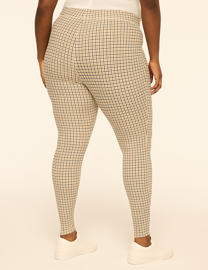 A person wearing plaid leggings and white sneakers stands against a plain, light-colored background.
