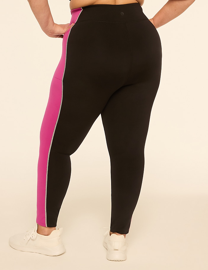 A person wearing black leggings with a pink stripe down the side stands against a plain, light-colored background.