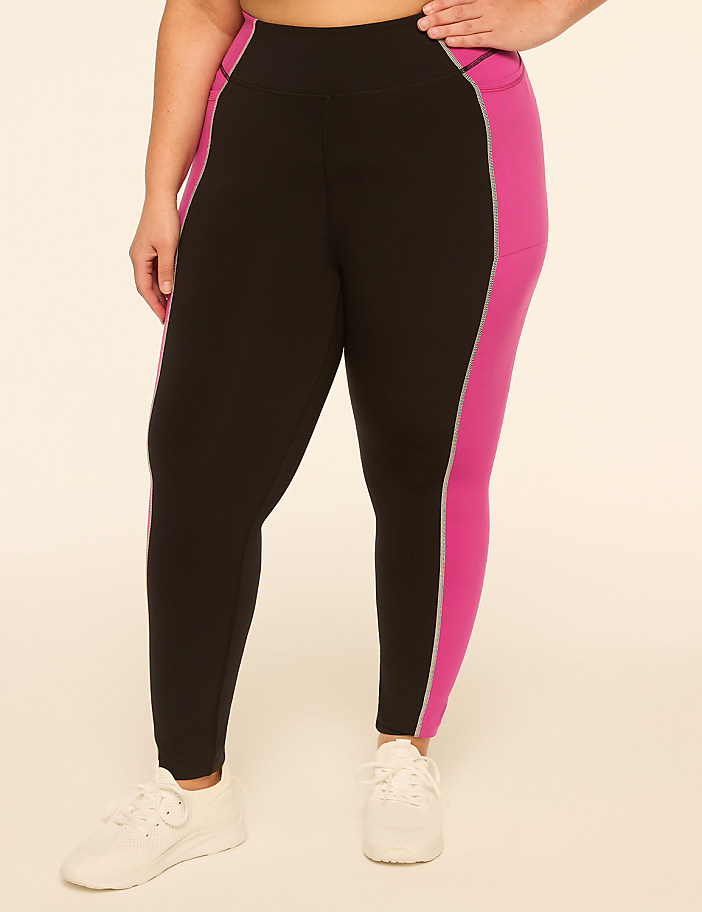 A person wearing black leggings with pink side panels and white sneakers stands against a plain, light-colored background.