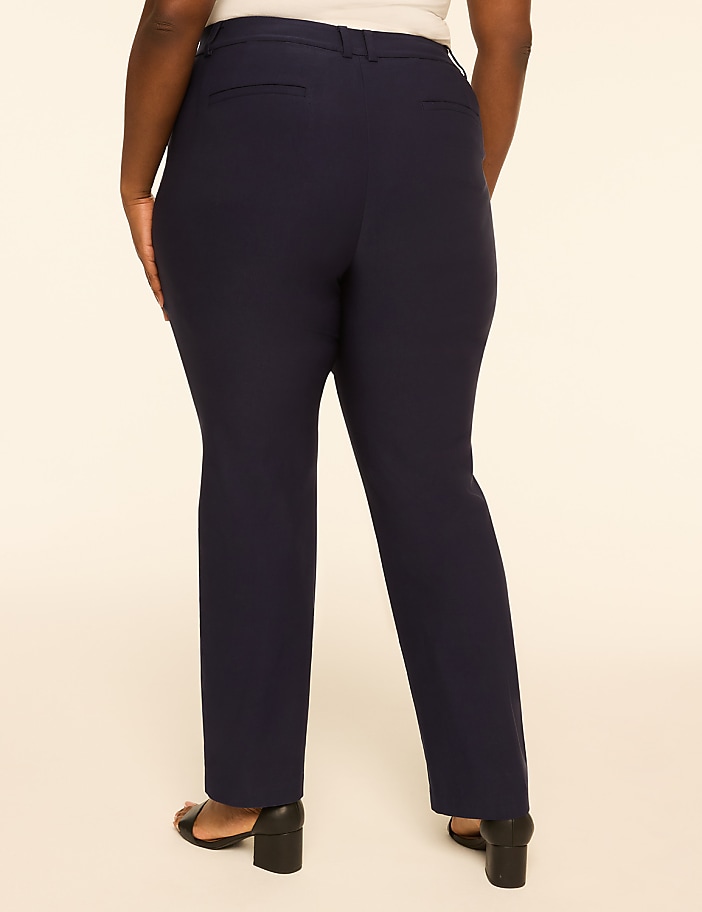 A person wearing navy blue dress pants and black heels stands against a plain, light-colored background.