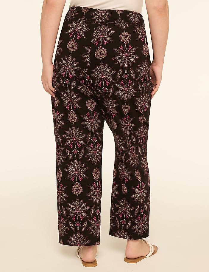 A person wearing patterned pants stands against a plain, light-colored background.