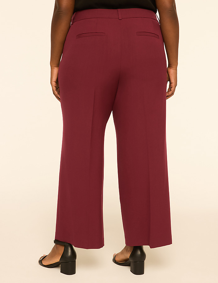 A person wearing burgundy wide-leg pants and black heels stands against a plain, light-colored background.