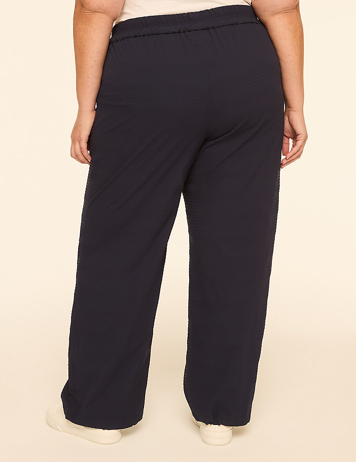 A person wearing dark blue, wide-leg pants stands against a plain, light-colored background.