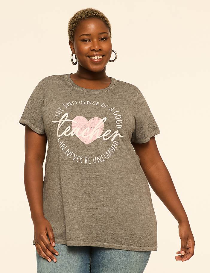 A smiling woman in a grey t-shirt with a teacher-themed graphic stands against a plain, light-colored background.