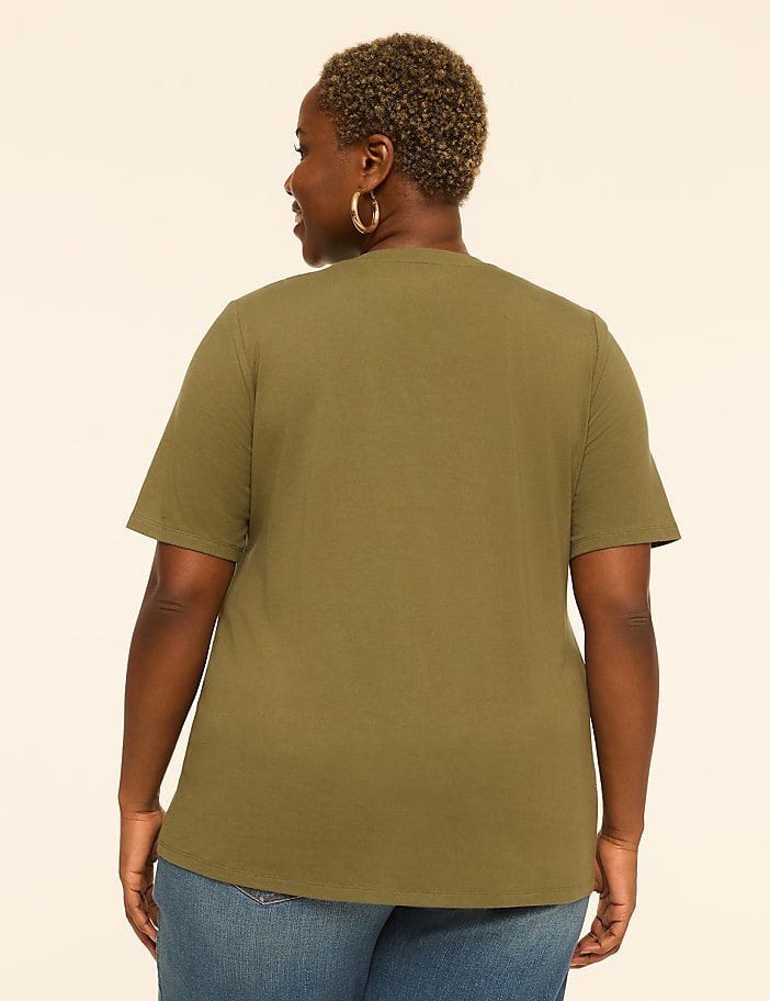 A woman in a green t-shirt and blue jeans stands against a plain, light-colored background.