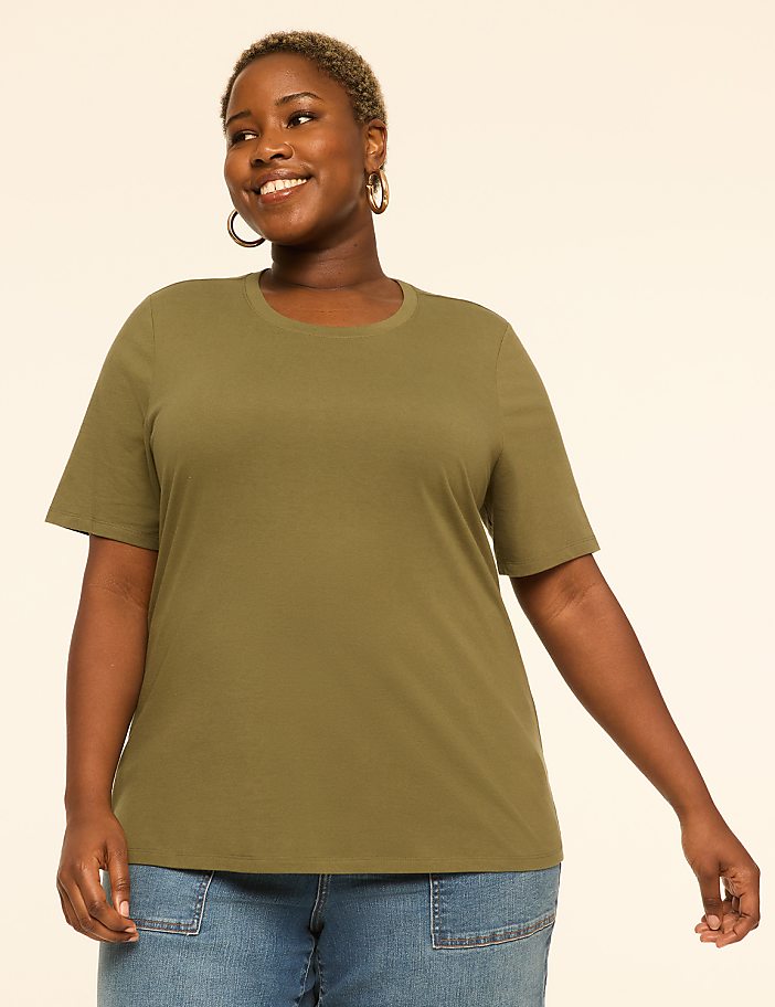 A smiling woman in a green t-shirt and blue jeans stands against a plain, light-colored background.