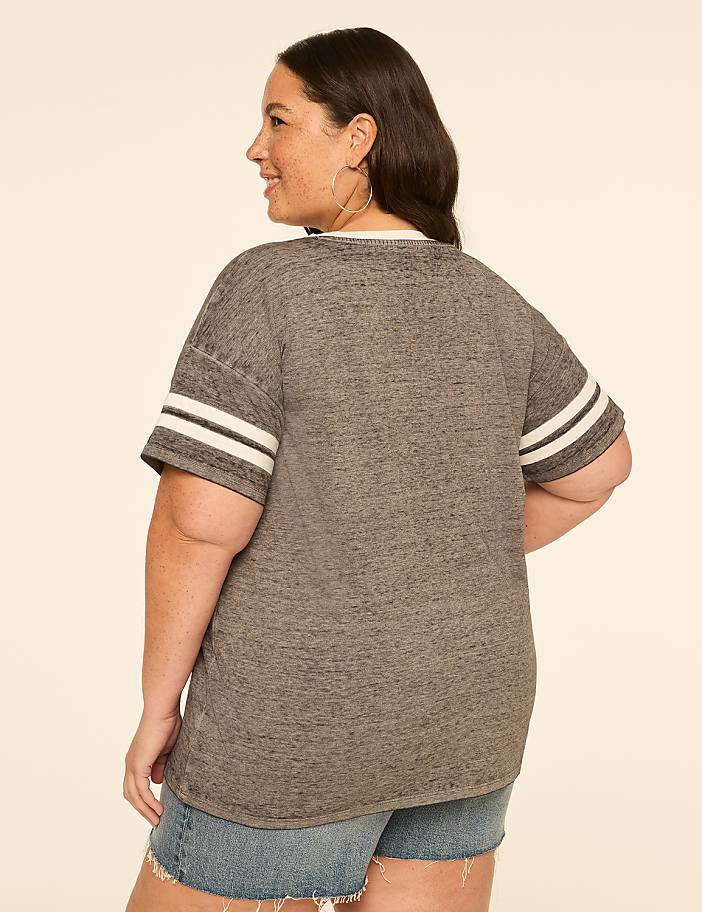 A woman in a grey t-shirt and denim shorts stands against a plain, light-colored background.