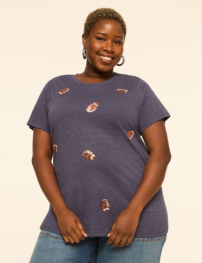 A smiling woman with short hair wears a navy blue t-shirt with football graphics, standing against a plain cream background.