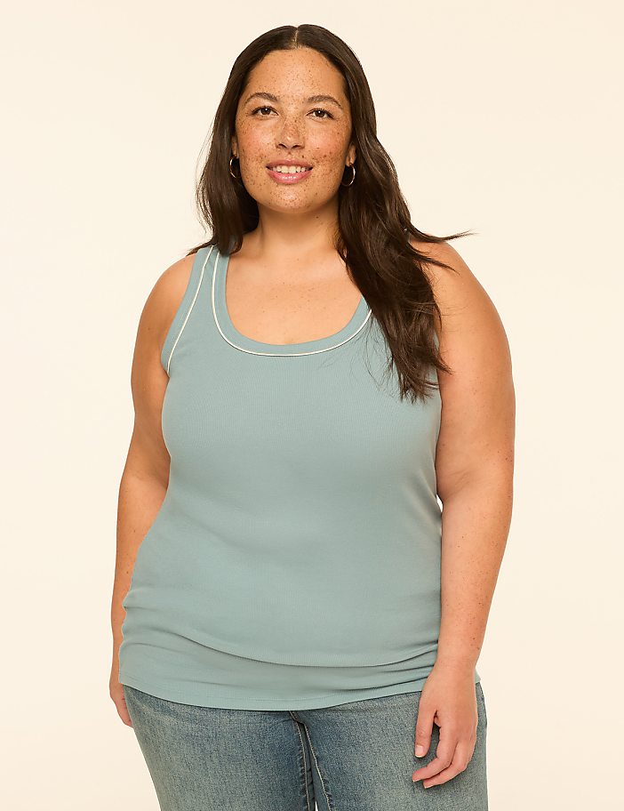 A woman in a light blue tank top and jeans stands against a plain, light-colored background.