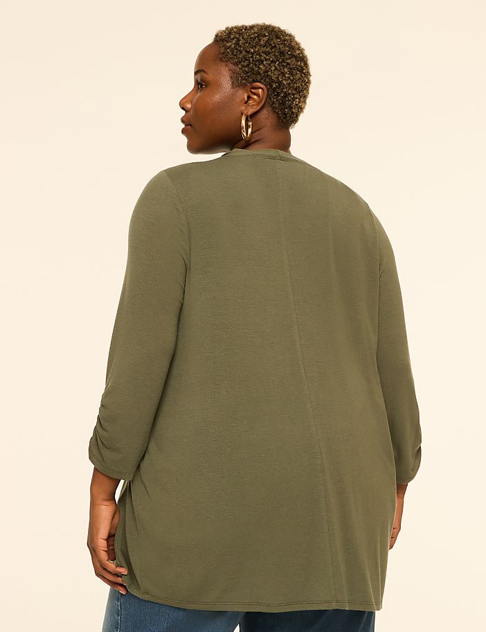 A woman in a green cardigan stands against a plain, light-colored background.