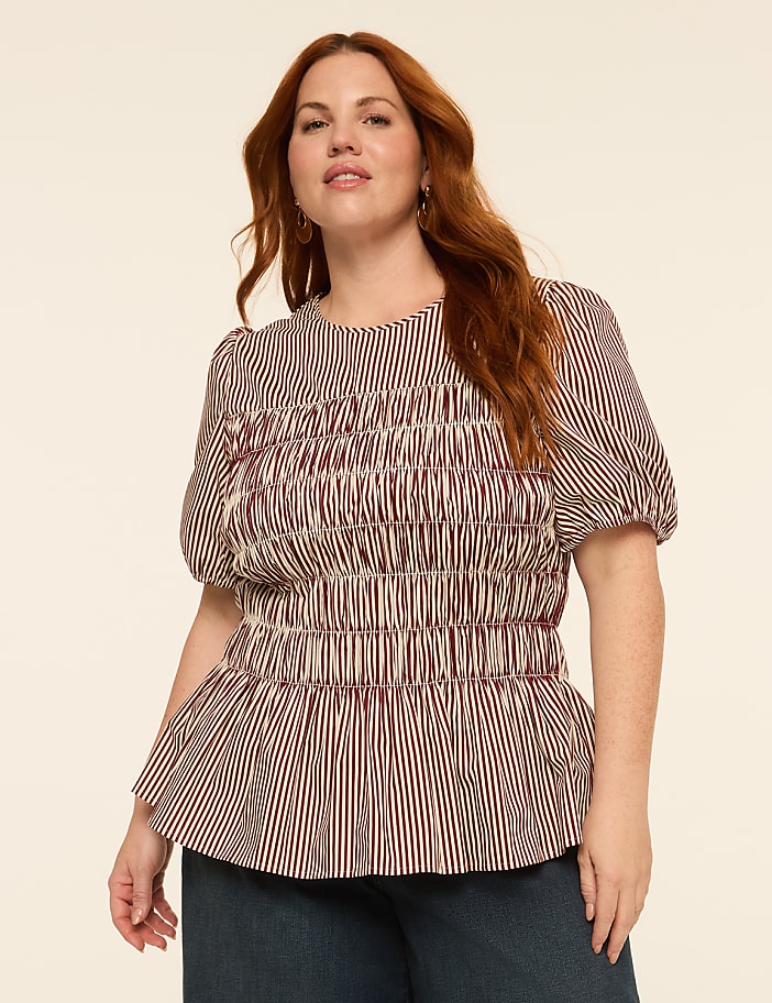 A woman with auburn hair and fair skin, wearing a red and white striped peplum top, poses against a plain, light-colored background.