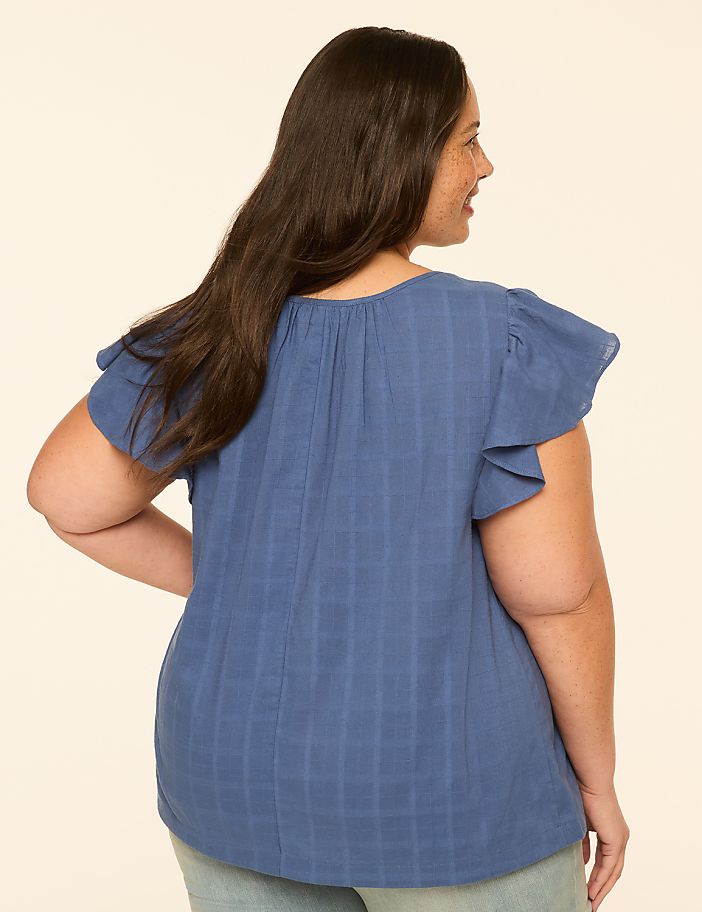 A woman in a blue, textured top with flutter sleeves is shown from the back against a plain, light-colored background.