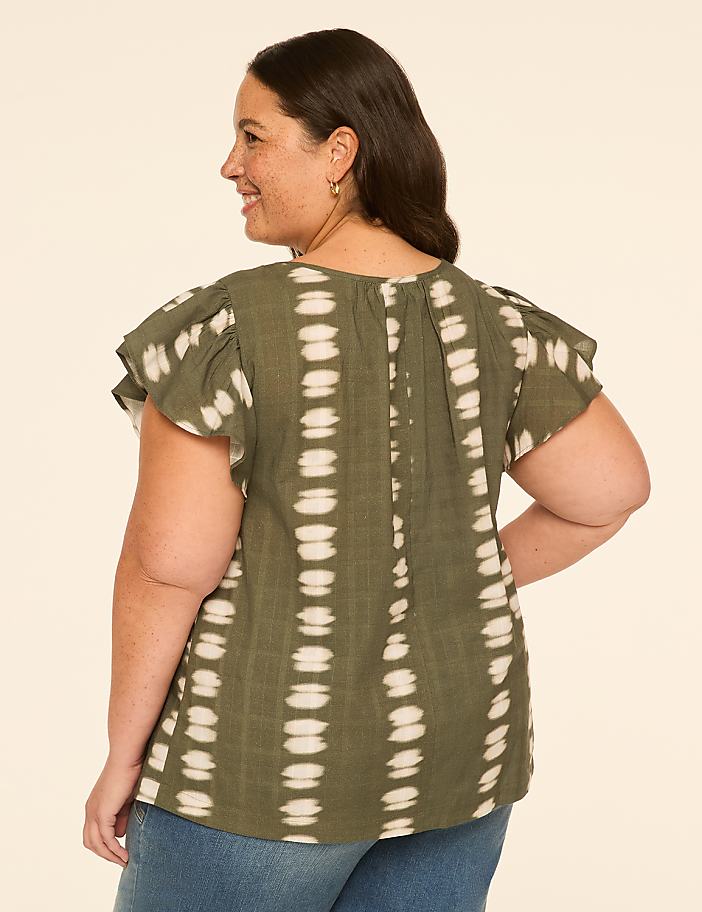 A woman in a green tie-dye top stands against a plain beige background.