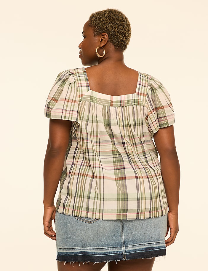 A woman in a plaid top and denim skirt stands against a plain, light-colored background.