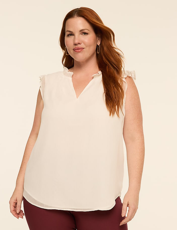 A woman with auburn hair and fair skin, wearing a cream-colored ruffled blouse and maroon pants, poses against a plain beige background.