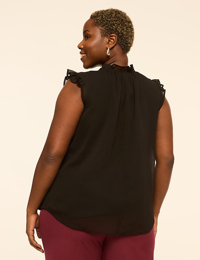 A woman in a black ruffled-sleeve blouse and maroon pants stands against a plain, light-colored background.