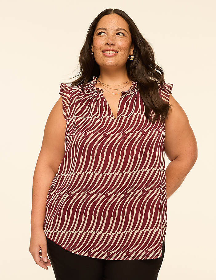 A woman with dark hair and a patterned blouse stands against a plain, light-colored background.