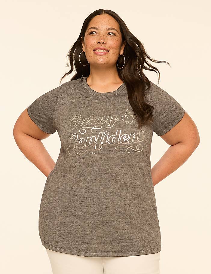 A woman with dark hair and hoop earrings smiles confidently in a grey t-shirt with "Curvy & Confident" written on it, set against a plain, light-colored background.