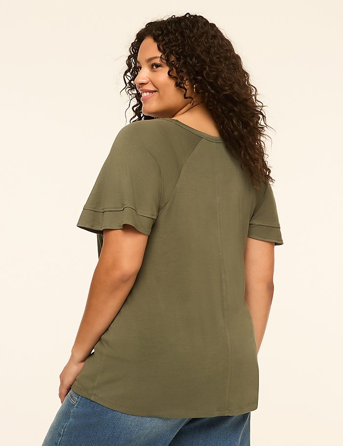 A woman in a green t-shirt and blue jeans stands against a plain, light-colored background.
