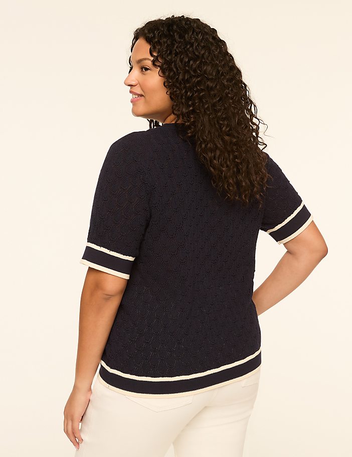 A woman in a navy blue sweater with white trim stands against a plain, light-colored background.