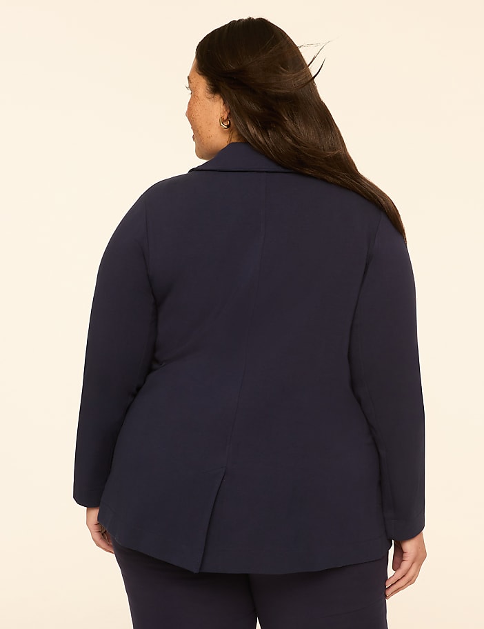 A woman in a navy blazer and pants stands with her back to the camera against a plain, light-colored background.