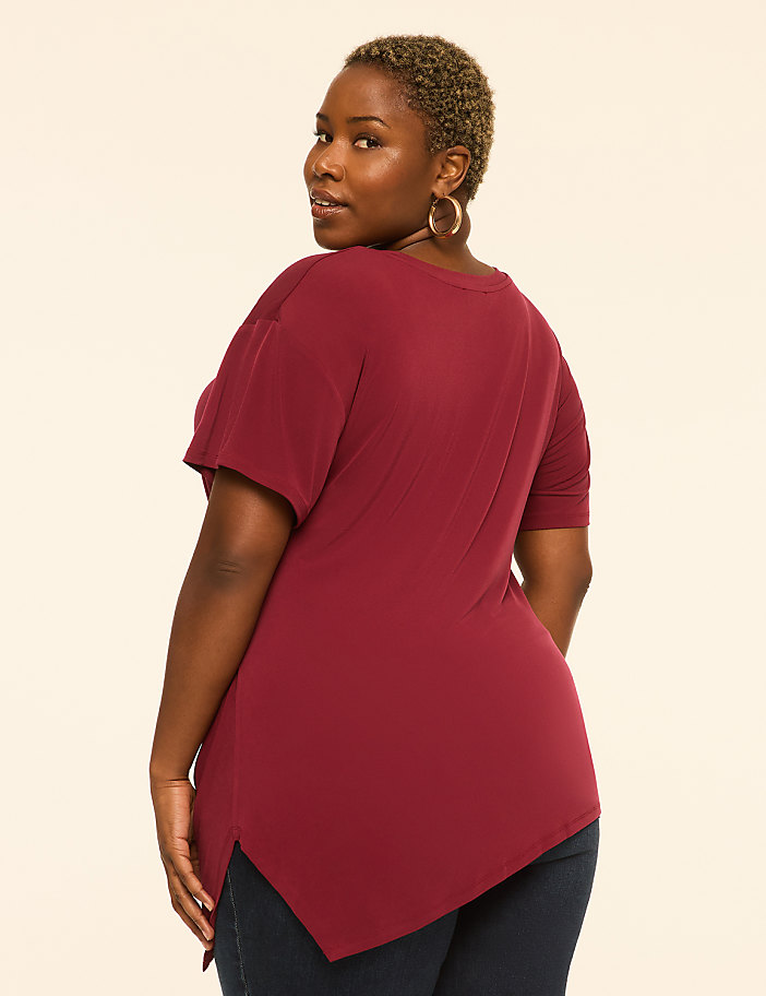 A woman in a maroon tunic and dark jeans stands against a plain, light-colored background.